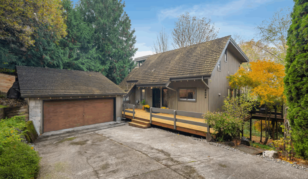 Front view of a Pacific Northwest-style home in Seattle with wooden deck, detached garage, and mature landscaping